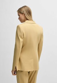 Yellow blazer with a structured design, notch lapels, and two back vents. Smooth texture and tailored fit.