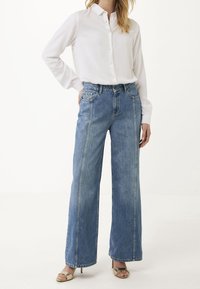 Ljust blå vida jeans i denim med hög midja, stora framfickor och rak silhuett, kombinerat med en vit skjorta.