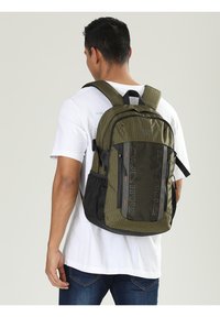 Zaino verde oliva con tessuto testurizzato, dettagli neri, diversi scomparti, spallacci regolabili e fondo rinforzato per una maggiore durata.