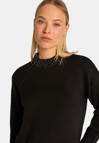 Czarny sweter dzianinowy z teksturowanym kołnierzem ozdobionym czarnymi koralikami, rękawami raglanowymi oraz dopasowanym krojem.