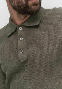 Olivgrön stickad pikétröja med texturerat tyg, knäppning med tre knappar och krage. Knapporna är runda med en fyrhålsdesign.