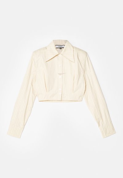 Chemise à manches longues coupée, de couleur beige clair avec des rayures verticales. Elle présente un col pointu, une fermeture par boutons et un tissu texturé.