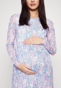 Umstandsabendkleid in Hellblau mit floralen Mustern in Rosa und Grün. Hergestellt aus weichem Stoff, mit langen Ärmeln und gerafftem Taillenbereich.