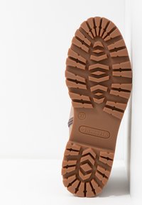 Semelle d'une botte marron avec des motifs de semelle profonds, taille 37 indiquée, et le nom de la marque "Tamaris" embossé sur la semelle.