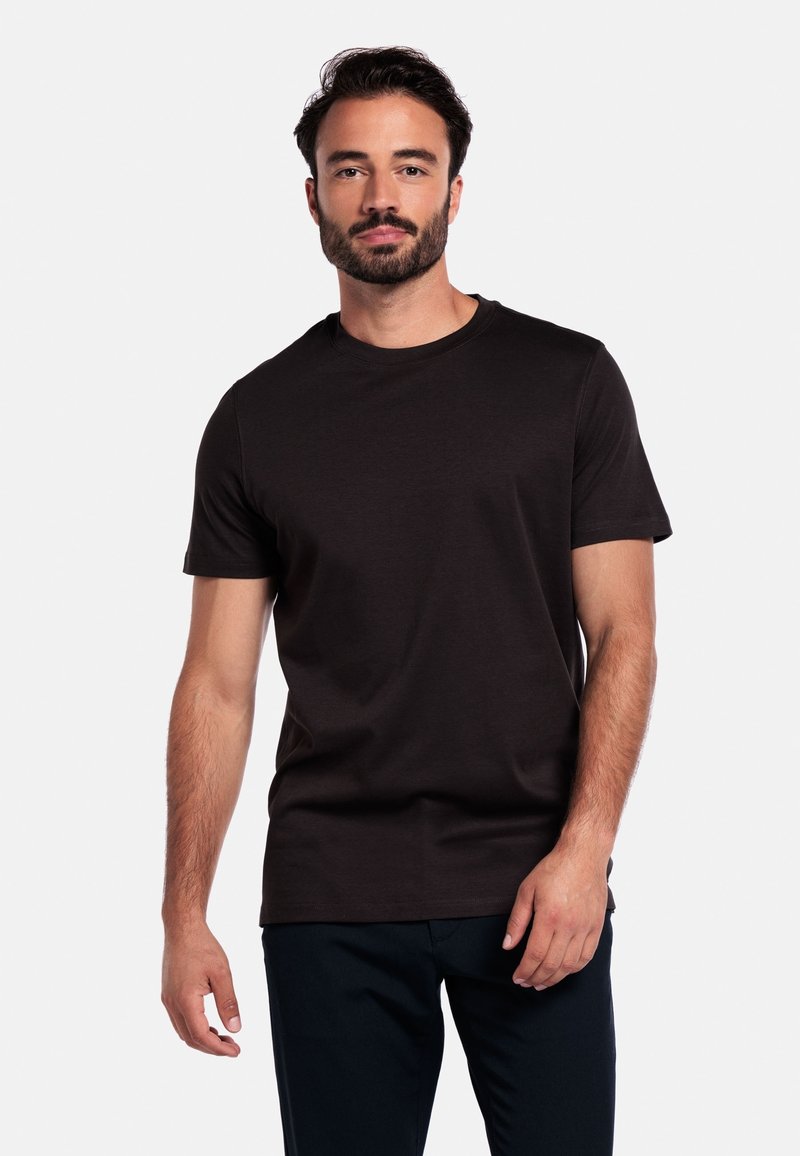 Donkerbruin kortemouwen t-shirt van zacht materiaal, met een ronde halslijn en een relaxte pasvorm. Gekocht in combinatie met marineblauwe broeken, wat een casual stijl benadrukt.