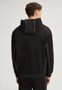 Zwarte hoodie met capuchon, met witte contrasterende lijnen langs de zijden en manchetten. Gemaakt van zachte stof, ontworpen voor comfort.