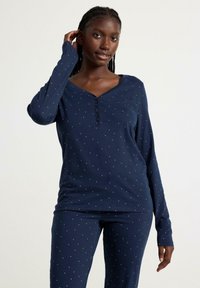 Ensemble de pyjama bleu marine à manches longues, avec un col henley et un petit motif à pois blancs. Tissu doux avec une texture lisse.