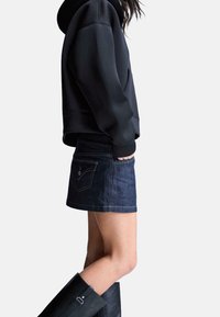 Sweat-shirt à capuche noir, mini-jupe en jean, et bottes noires montant jusqu'aux genoux. La tenue comprend des poches et une coupe ajustée.