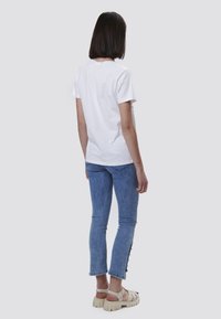 Camiseta blanca de algodón combinada con jeans de mezclilla azules que cuentan con botones laterales y sandalias de plataforma beige con múltiples tiras.