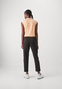 Short-sleeve peach top with a collar, paired with black cropped trousers. The outfit features a smooth texture and is complemented by white sneakers.