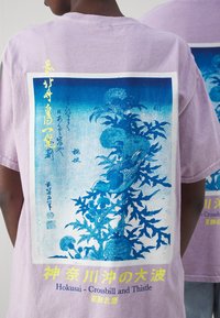 Lavendel bomull t-shirt med ett grafiskt tryck av törne och en fågel i blått och vitt, med gult text som gör designen.