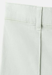 Lysegrønt denimstof med en glat tekstur, der har en enkel linning og ton-i-ton syninger. Fokus på dets rene linjer og minimalistiske design.