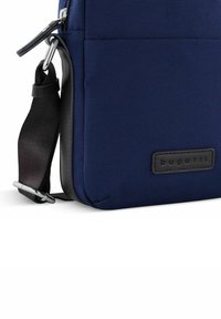 Borsa a tracolla in tessuto blu navy con dettagli in pelle nera, dotata di tracolla removibile, chiusura con cerniera e logo inciso sulla parte anteriore.