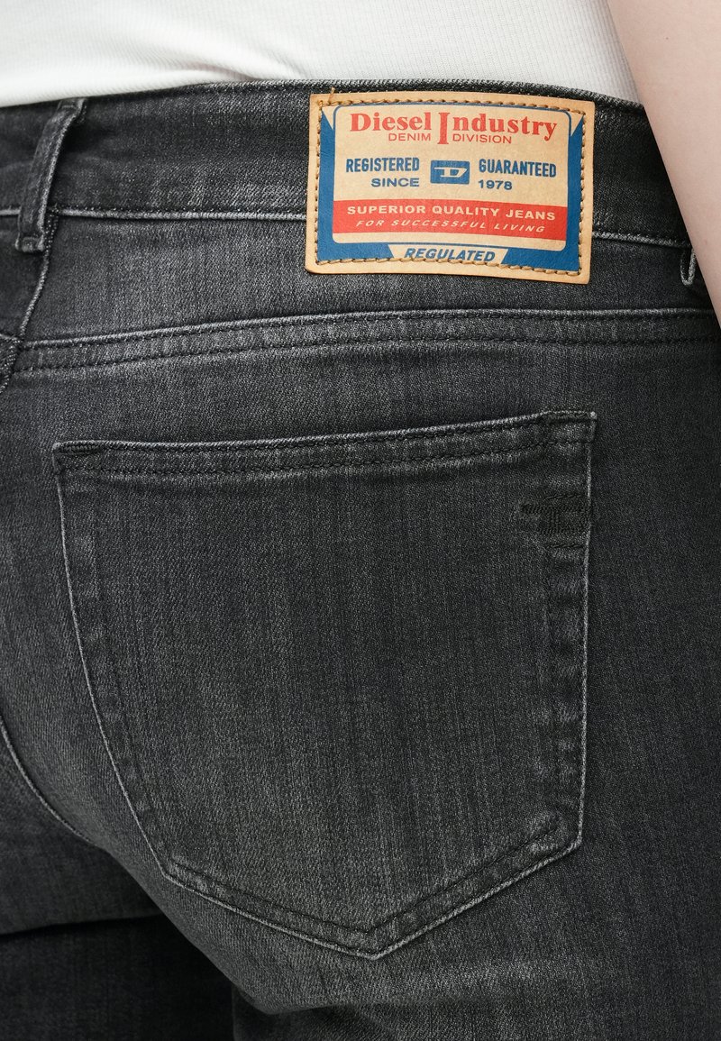 Grijze spijkerbroek van denim met een leren patch met blauwe en rode branding. Zichtbare stiksels en zakken verbeteren het ontwerp.