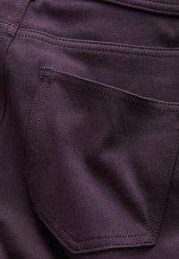 Donkerpaarse denimstof met een enkele achterzak met zichtbare stiksels en een gladde textuur. De stof heeft een lichte glans.