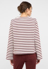 Langärmeliges gestreiftes Hemd mit abwechselnden Burgunder- und Cremestreifen, Rundhalsausschnitt und lockerem Schnitt; kombiniert mit Burgunderhosen.