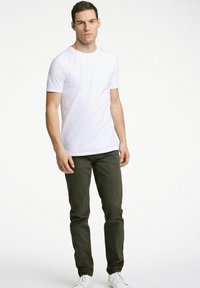Witte T-shirt met korte mouwen, gecombineerd met donkergroene slim-fit broek en witte sneakers. Het shirt heeft een ronde hals en een gladde textuur.