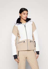 Beige und weiße Skijacke mit strukturiertem Finish, ausgestattet mit einem schwarzen Kunstfellkragen, Reißverschlüssen und kontrastierenden schwarzen Akzenten.