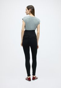 Sivý rebrovaný top s krátkym rukávom, čierne džínsy s vysokým pásom, priliehavý strih, zadné vrecká a lesklé červené topánky s plochou podrážkou.