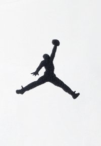 Musta kirjailtu Jumpman-logo valkoisella kangaspohjalla, jossa on dynaaminen asento, jossa jalat ja kädet ovat ojennettuina ja mukana on koripallo.