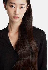 Czarna bluzka z dekoltem w serek. Długie, proste, ciemnobrązowe włosy opadające na jedno ramię. Gładka skóra w naturalnych odcieniach.