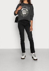 Sudadera gráfica negra con diseño floral, combinada con jeans negros ajustados y botas blancas con cordones y suela gruesa. Se incluye un bolso negro.