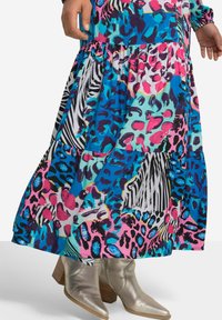 Robe maxi dans des motifs vibrants bleus, roses et verts, featuring des imprimés animaliers et une conception en niveaux. Assortie à des bottes à talons argentées brillantes.