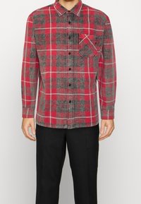 Camicia a maniche lunghe a quadri rossi e grigi in flanella, con chiusura a bottoni e tasca frontale. Caratterizzata da orlo dritto e colletto.