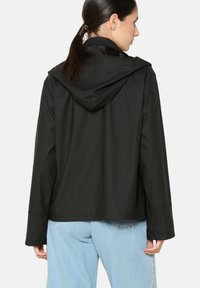 Juodas gobtuvas striukė, pagaminta iš lygios medžiagos, su ilgomis rankovėmis, laisvu kirpimu ir tiesiu apdailos kraštu. Atgalinis vaizdas be matomų akcentų.