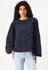 Blusa blu navy con motivo floreale, scollatura rotonda e maniche lunghe voluminose. Realizzata in tessuto leggero con una texture morbida.