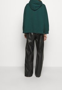 Teal oversized hoodie med huva och ribbade manschetter, kombinerad med svarta byxor i konstläder med vida ben, som har en slät textur och avslappnad passform.