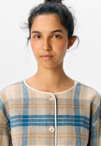 Cardigan a quadri con tonalità blu, beige e arancione. Realizzato in tessuto morbido, presenta un colletto rotondo, chiusura con bottoni e rifiniture a contrasto.