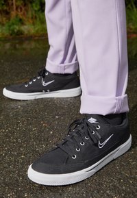 Svarta canvas sneakers med en vit gummisula. Har grå snörhål, svarta snören och en vit Nike-logotyp på sidan.