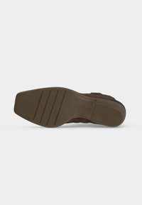 Semelle d'une chaussure en cuir marron avec des motifs de grip texturés comprenant des rainures horizontales et une partie de talon côtelée.