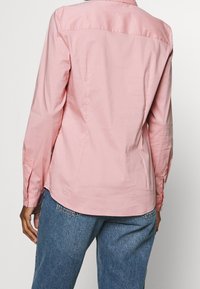 Ljusrosa långärmad skjorta med klassisk krage och knäppta manschetter, med en slät textur och en figurnära design längs ryggen.