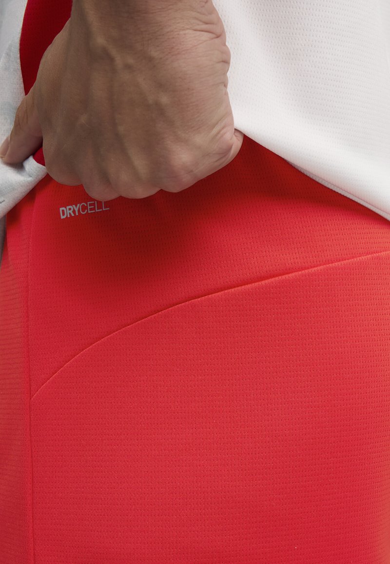 Leggings de rendimiento rojos con una tela texturizada que cuenta con una propiedad de absorción de humedad etiquetada como "DRYCELL", combinados con una camiseta blanca.