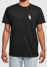 Schwarzes Baumwoll-T-Shirt mit einem weißen Grafikdesign, das eine Hand zeigt, die eine Herzgeste macht, und einem roten Herzakzent auf der linken Brustseite.