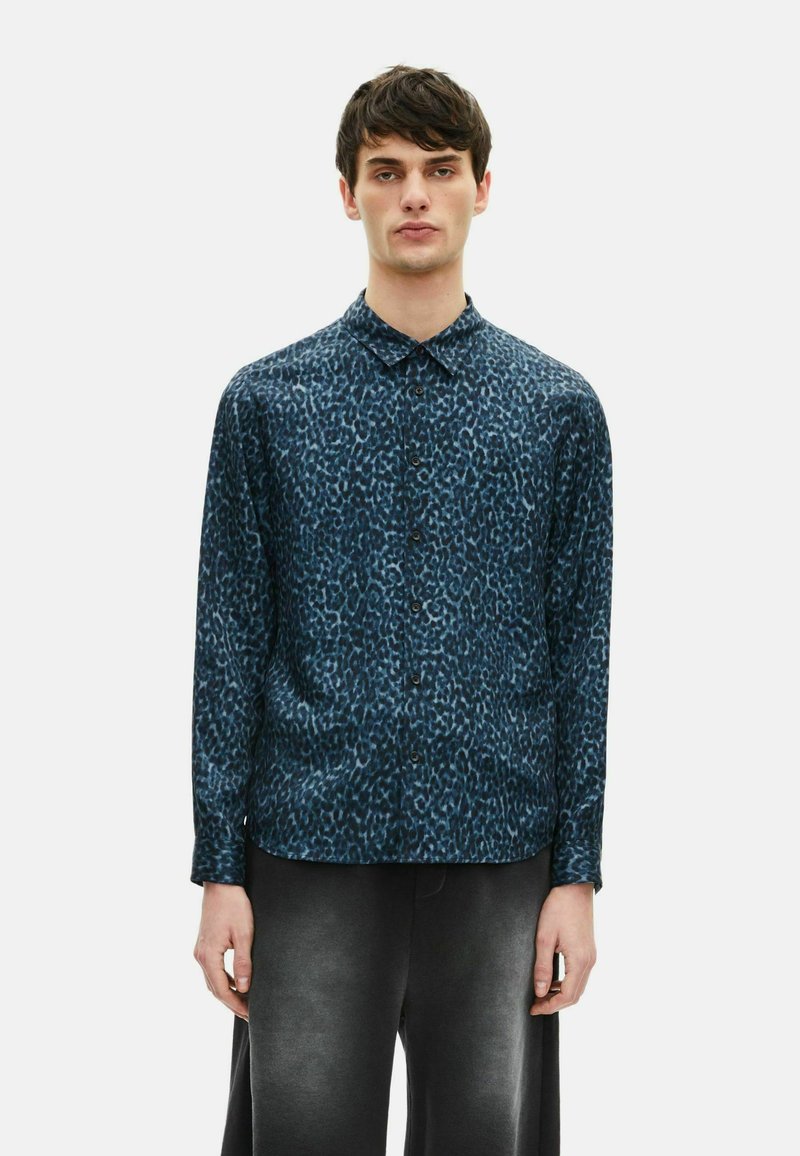 Leopardprint shirt in donkerblauw en zwart; lange mouwen, knoopsluiting aan de voorkant en lichtgewicht textuur. Gepaarde met donkergrijze broek.