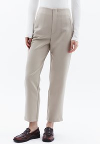 Beige hoge taille broek met verticale plooien, rechte benen en zijzakken. Gestyled met donkerbruine instapschoenen. Glad stoftextuur.