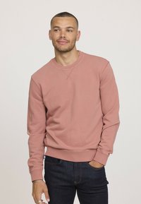 Sweatshirt rose en tissu doux, doté de manches longues, d'un col rond et de poignets côtelés. Porté sur un jean bleu foncé. Sans motifs ni accents.