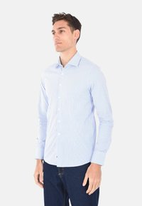 Camicia a maniche lunghe a righe blu chiaro e bianche, con bottoni, colletto a punta e vestibilità sartoriale, abbinata a jeans in denim scuro.