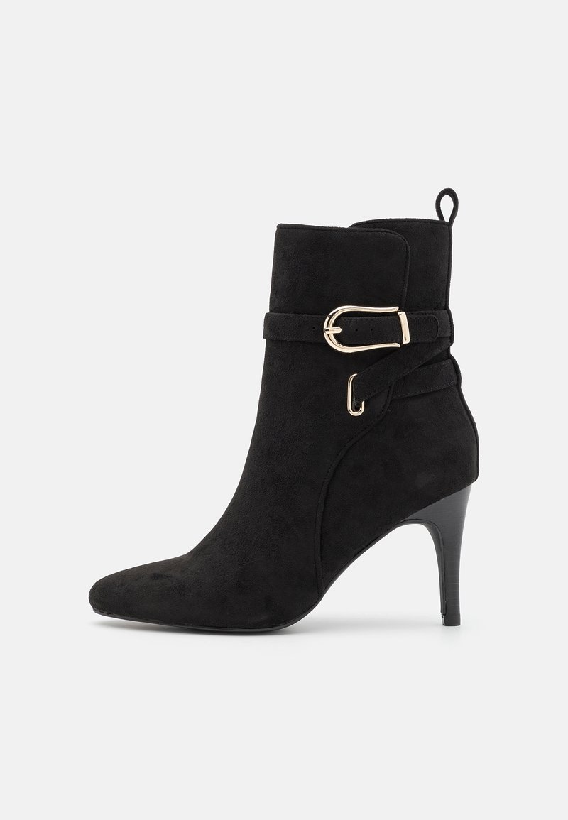 Bottine en daim noir avec bout pointu, talon haut et fin, bride décorative à boucle dorée et languette d'extraction à l'arrière.