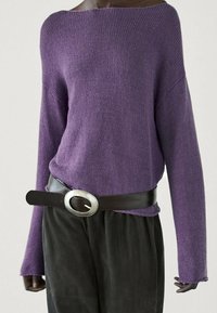 Pull en tricot violet avec un design à épaules dénudées, manches longues, associé à un pantalon noir à jambes larges et une ceinture marron avec une boucle circulaire en argent.