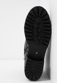 Semelle de botte noire avec des sculptures profondes et des motifs en forme de croix, taille de chaussure 37 visible sur une surface plane blanche et dans un coin de mur.