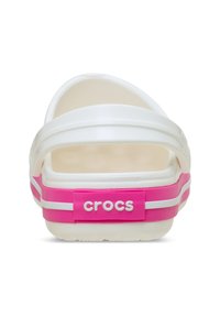 Białe i różowe klapki Crocs widziane z tyłu, z białą rączką i różowym obcasem, z logo "crocs" w białych literach.