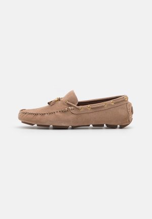 Chaussure mocassin en daim beige avec un bout arrondi, un laçage décoratif et des œillets dorés. Semelle en caoutchouc avec de petites rainures pour l'adhérence.