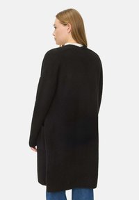 Langer schwarzer Cardigan aus einem weichen, strukturierten Stoff, mit lockerer Passform, überschnittenen Schultern und seitlichen Taschen.