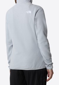 Chaqueta de forro polar gris claro con cuello alto, que presenta un logo sutil en la parte superior de la espalda y una tela texturizada. Mangas largas y ajuste recto.