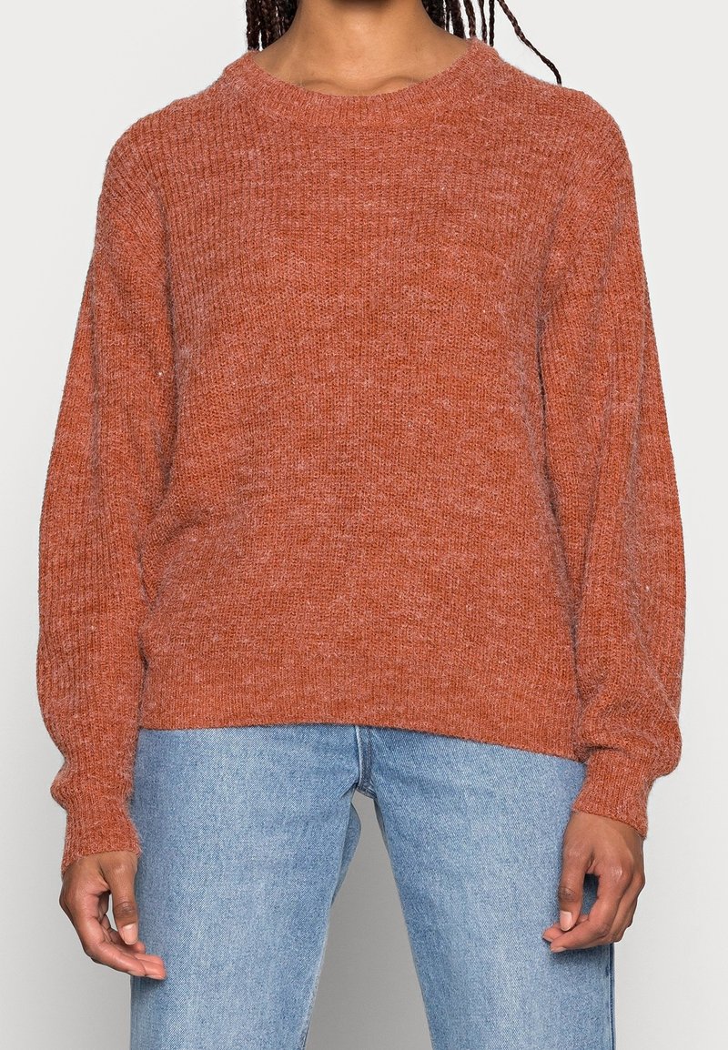 Pull en maille couleur rouille avec un col rond, des manches longues et une coupe décontractée, associé à un jean en denim bleu clair.