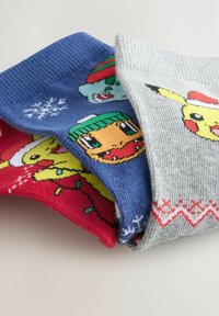 Kolme taiteltua juhlasukkaa, joissa on Pikachu, Squirtle ja Bulbasaur talvihatuissa ja joulukoristeilla punaisilla, sinisillä ja harmailla taustoilla.